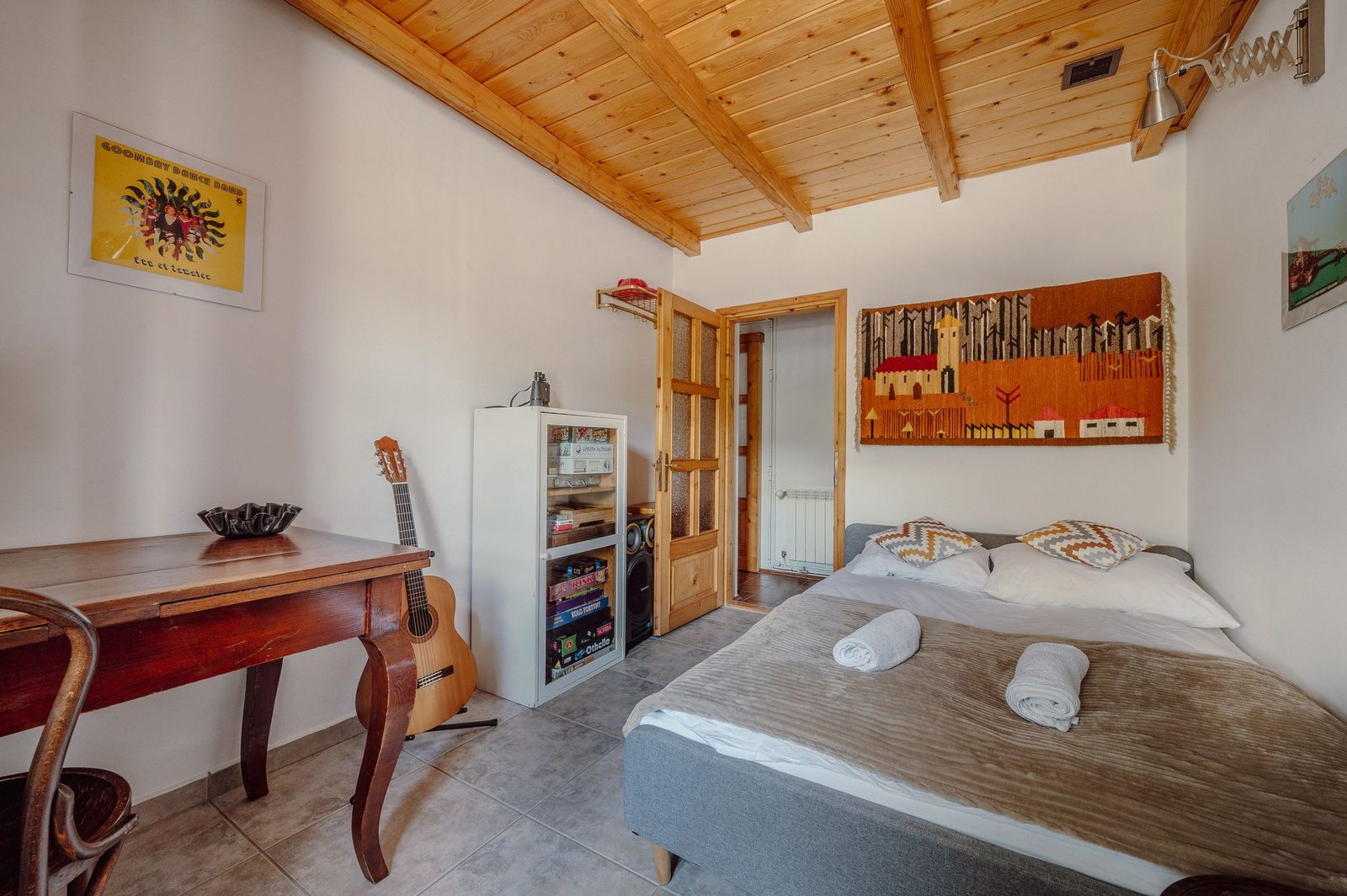 Room with a timber-beamed ceiling, a double bed, an old wooden table and a guitar