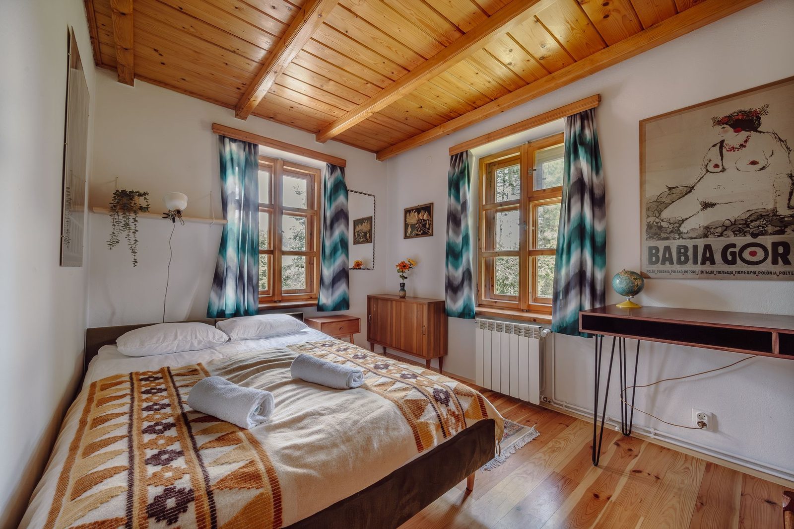 Bedroom with a wooden ceiling, two curtained windows and a poster of Babia Góra